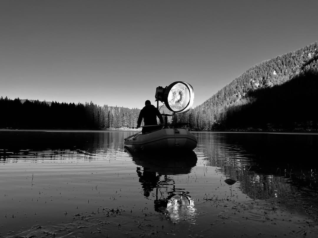Black-and-white lake at dawn with a technician lighting from an inflatable boat
