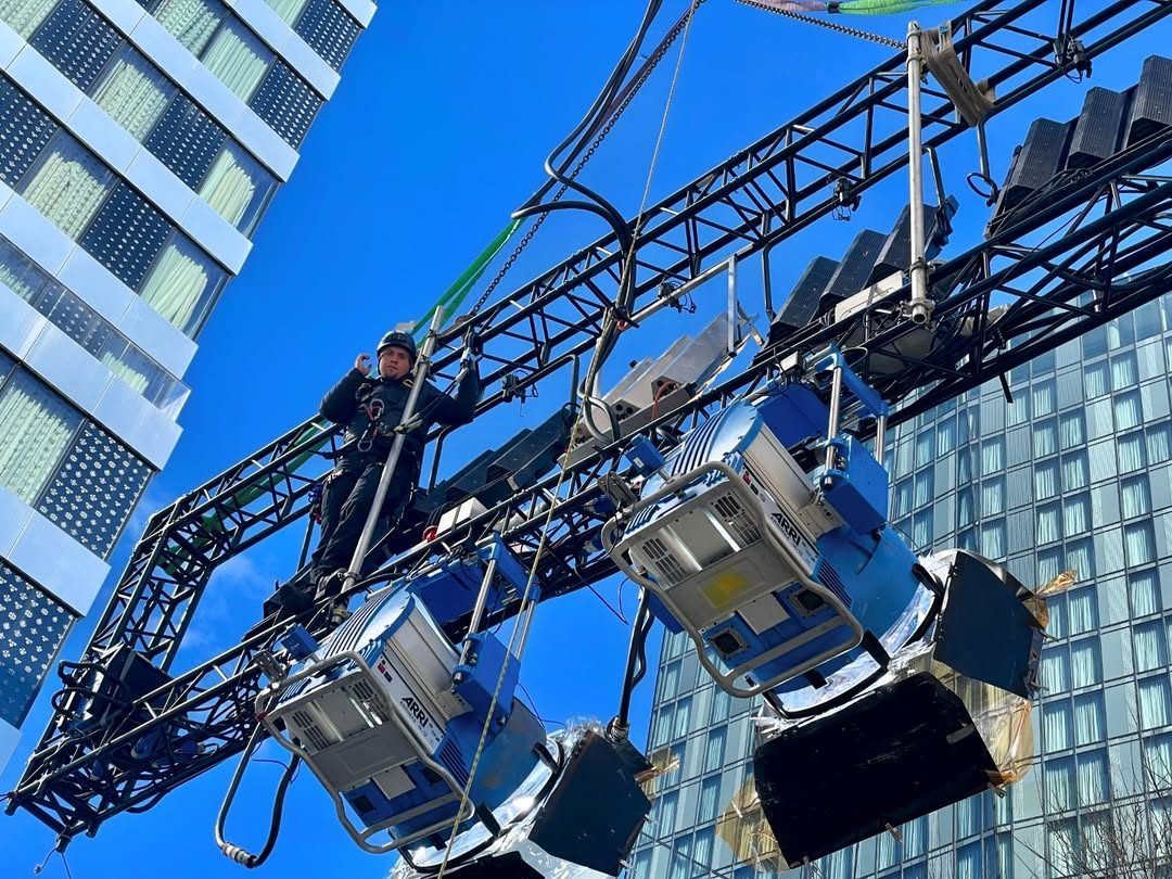 Looking up at fixtures on a truss against a skyscraper and blue sky