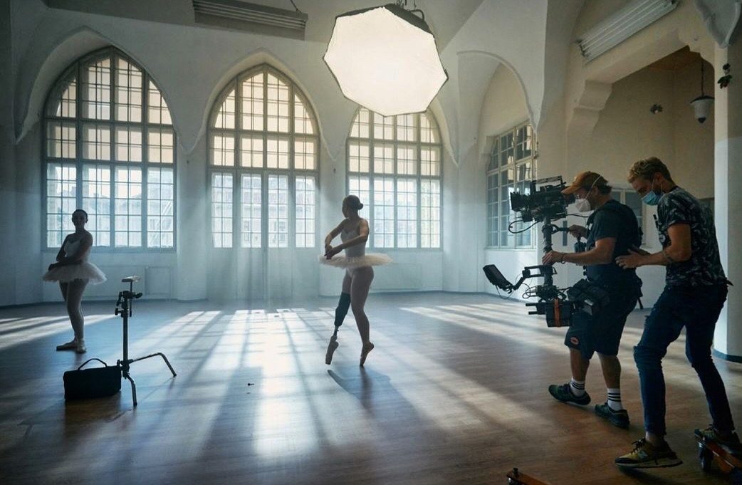 Ballet dancers filmed in a sunlit hall with arched windows