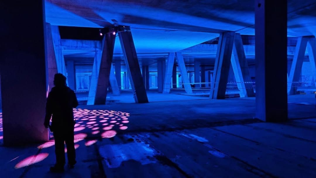 Figure under concrete pillars lit blue with a pink gobo on the floor