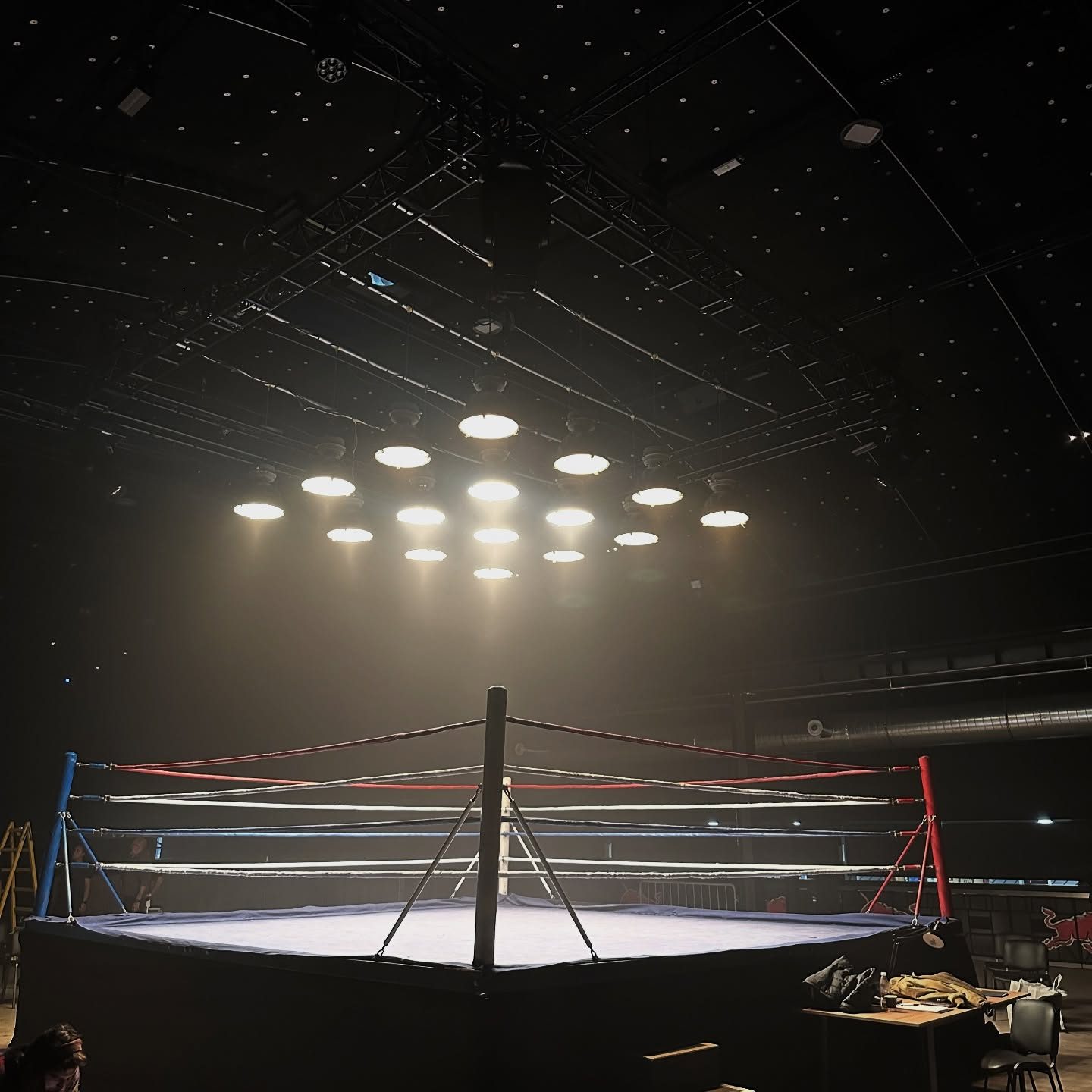 Boxing ring under a rig of practical lights in a dark studio