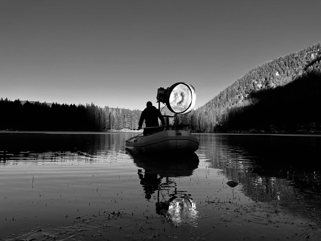 Black-and-white lake at dawn with a technician lighting from an inflatable boat