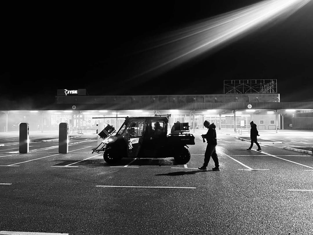 Crew and a telehandler on a wet forecourt at night, black and white