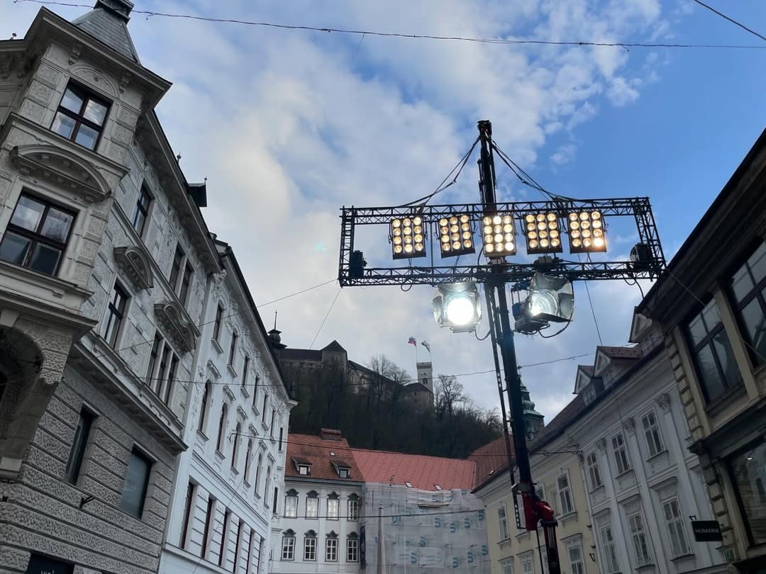 Crane-mounted light array over an old town street below a castle