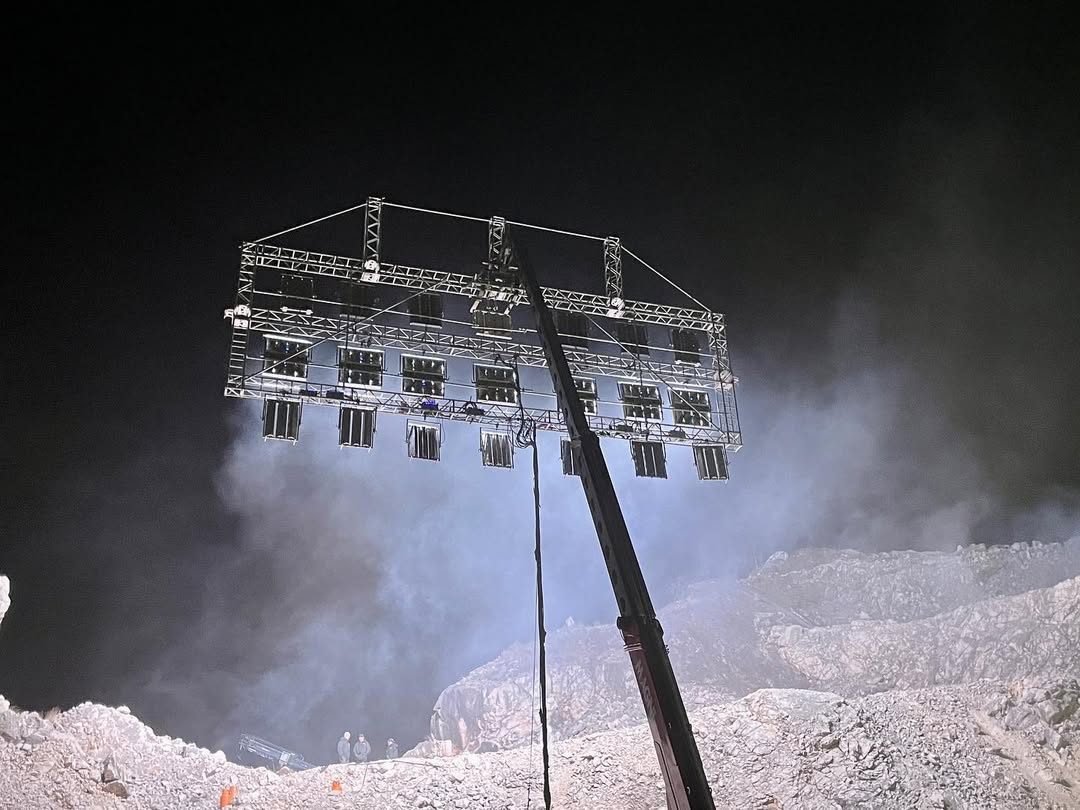 Crane lifting a lighting truss through dust in a quarry