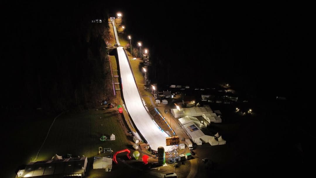 Aerial night view of a floodlit ski jump and event grounds