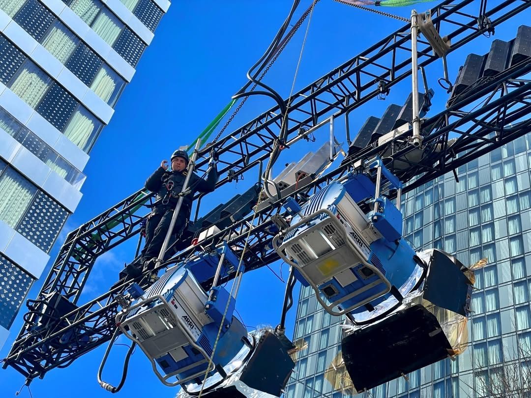 Looking up at fixtures on a truss against a skyscraper and blue sky