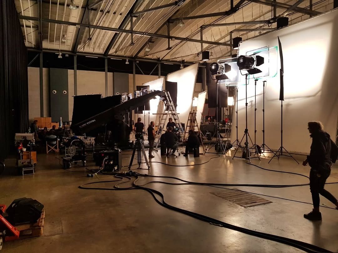 Crew building a white-cyclorama studio set with tungsten fixtures